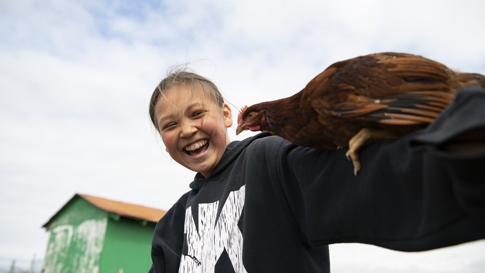 A girl smiles and laughs at the chicken perched on her arm