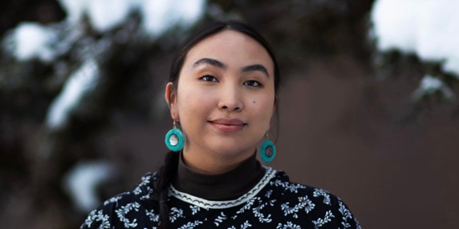 Charitie Ropati looks at the camera wearing a dark shirt with leaves on it and turquoise earrings