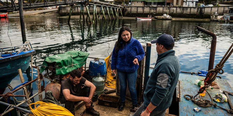 A fisherwoman speaks to 2 men on deck