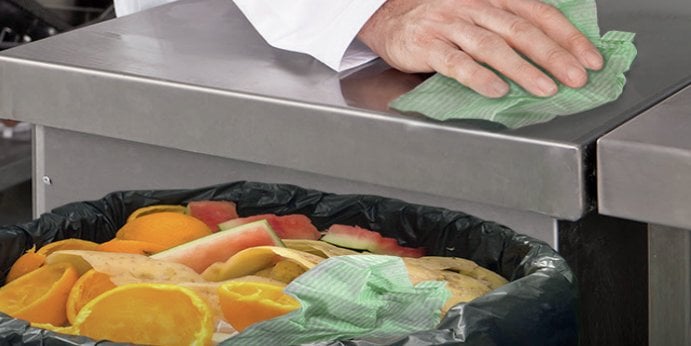 A bin holding composted food items next to a metal professional kitchen counter.