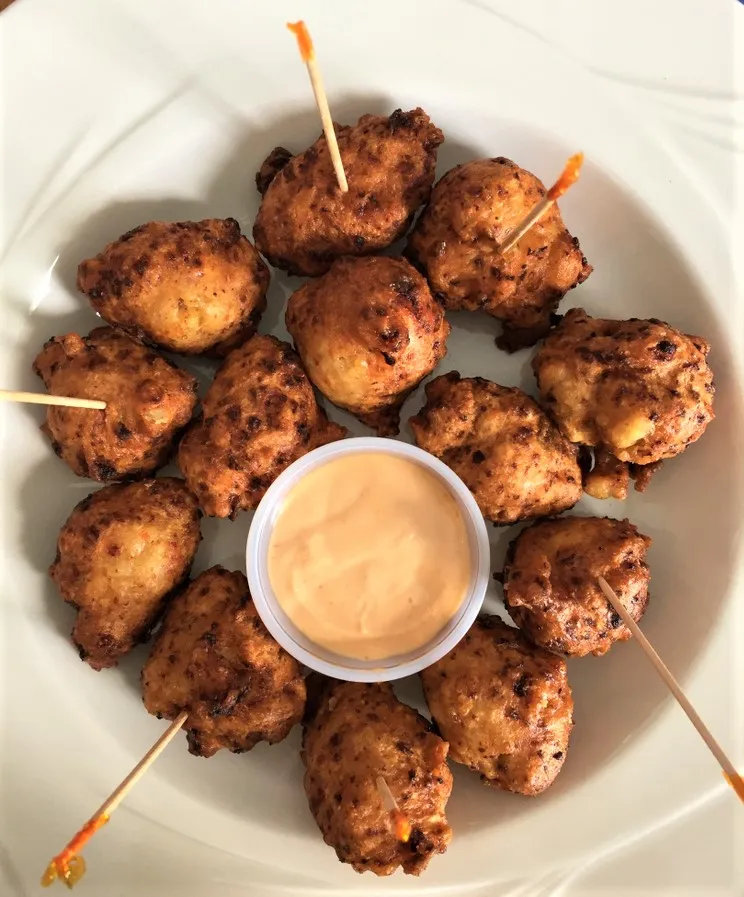 A plate of conch fritters with dipping sauce in the center