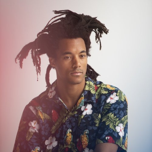 A headshot of a man in a flower button down shirt with dreadlocks