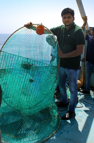 Un hombre sostiene una red de pesca grande, verde y redonda mientras está de pie en un barco.