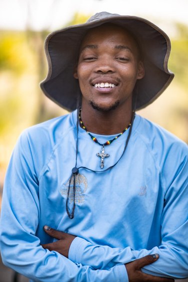 Cwi Cwi wears a blue shirt and a bucket hat and smiles at the camera