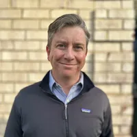 Headshot of Dan Riley smiling in a gray jacket
