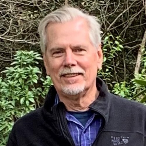 A headshot of a man in front of greenery