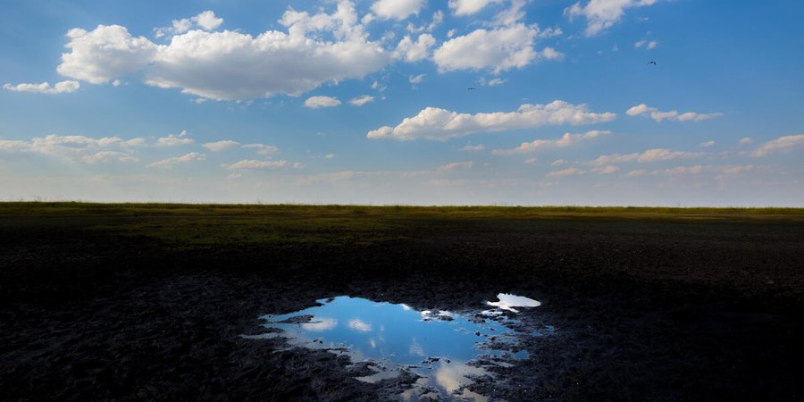A small bit of water reflects the blue sky and clouds in a mostly dried up fishing pan