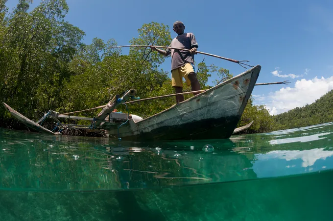 Split level of a shallow coral reef and mangroves with local West Papuan man and his wife in their dugout canoe