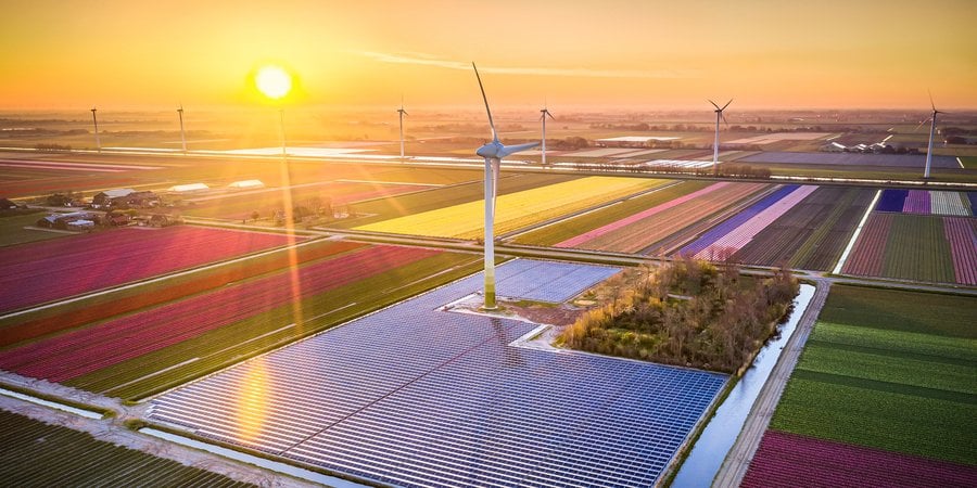 Windmills and solar panels in colorful fields at sunset