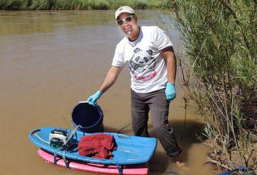 A photo of a man in a muddy river with measuring equipment on a small float