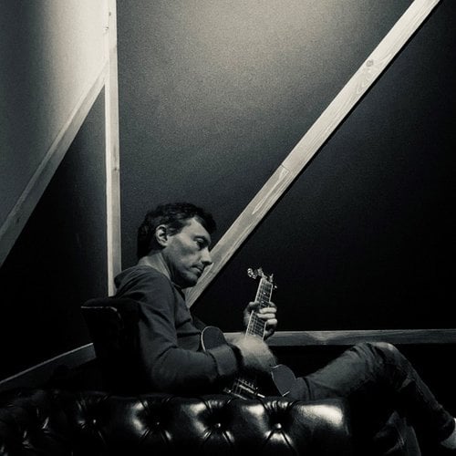 A black and white photo of a man sitting in a chair playing an electric guitar