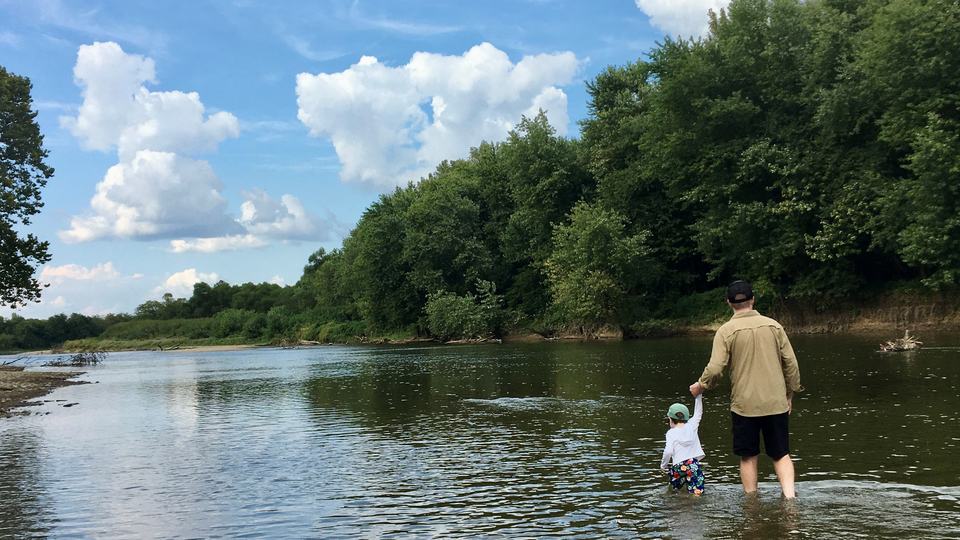 Evan and his child wading in a river