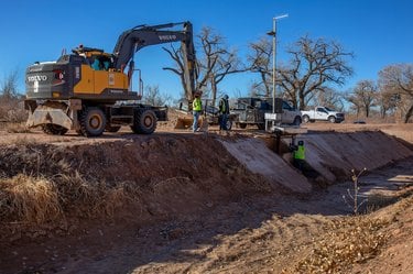 An excavator moving earth along ditch