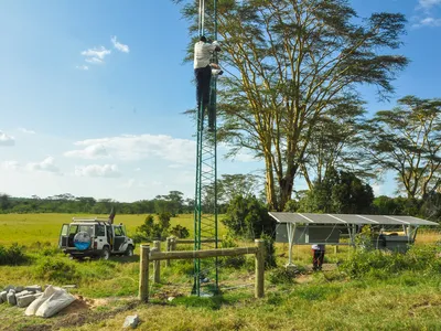 A man climbs a tower in a field to set up the FLIR nightvision camera