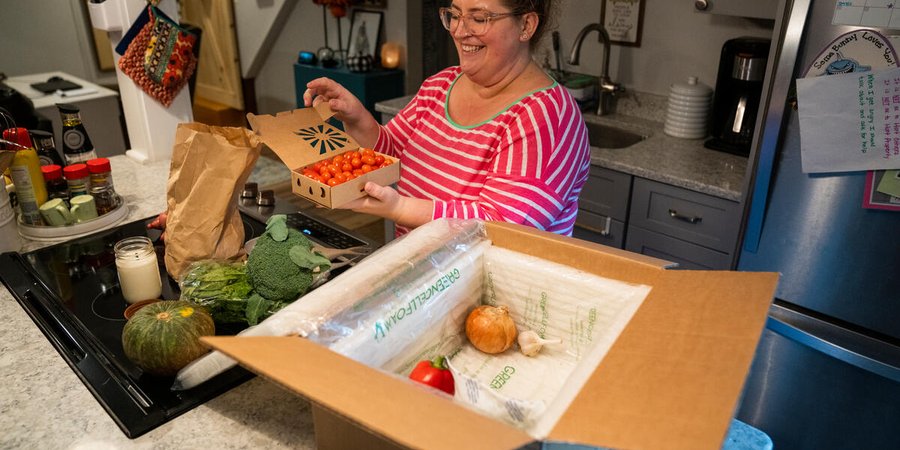 A person opens a box of fresh produce on her kitchen counter