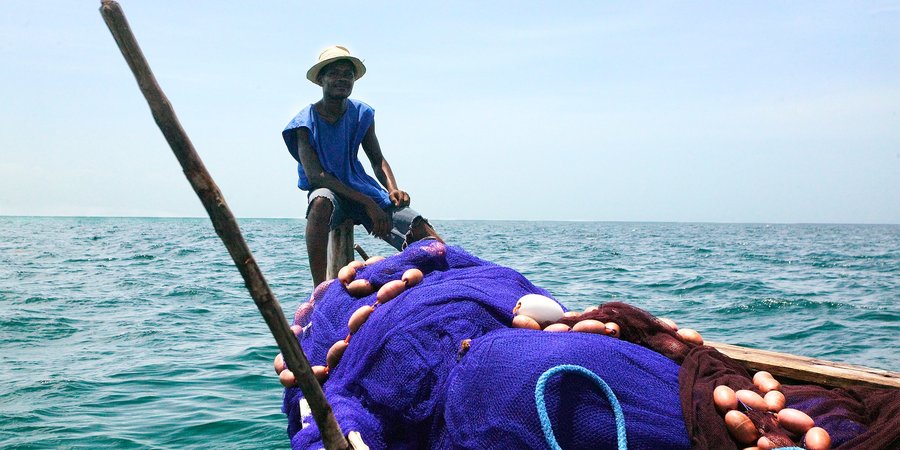 A fisher sits on the back of his boat, which is full of nets