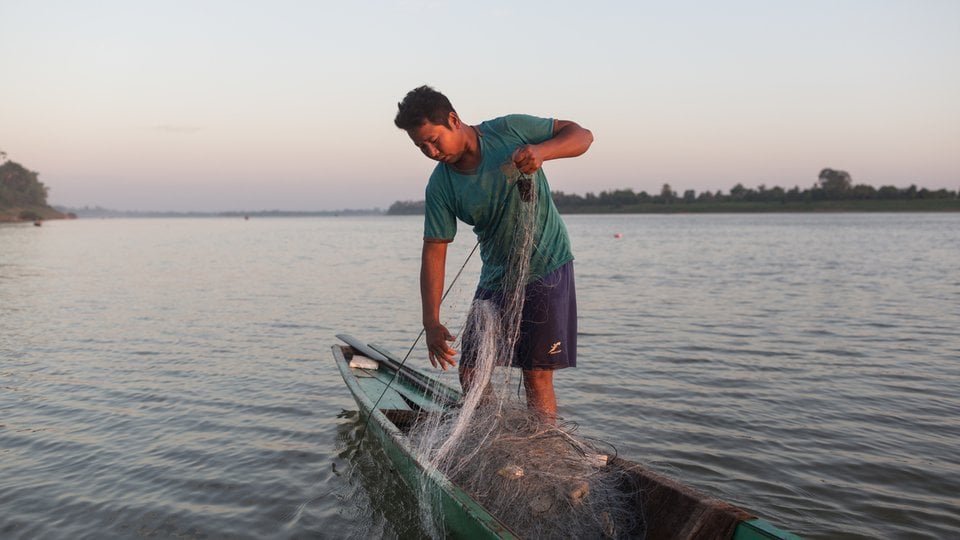A fisher pulls a net into a boat in low light