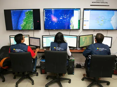 Three people sit in front of monitors showing various maps and data about fishing vessels