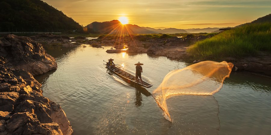 Two people cast a fishing net into the Mekong River as the sun rises
