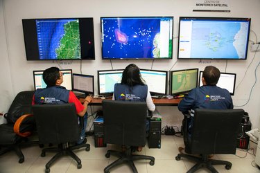 Three people sit in front of monitors showing various maps and data about fishing vessels