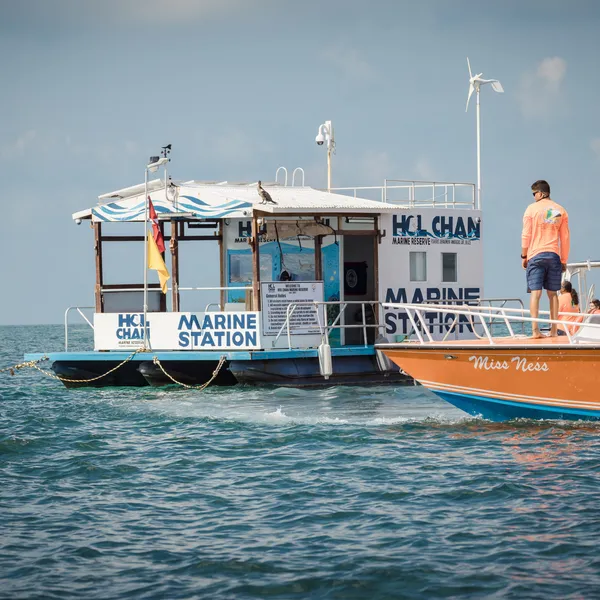 A floating ranger station is approached by an orange boat on a sunny day in Hol Chan, Belize