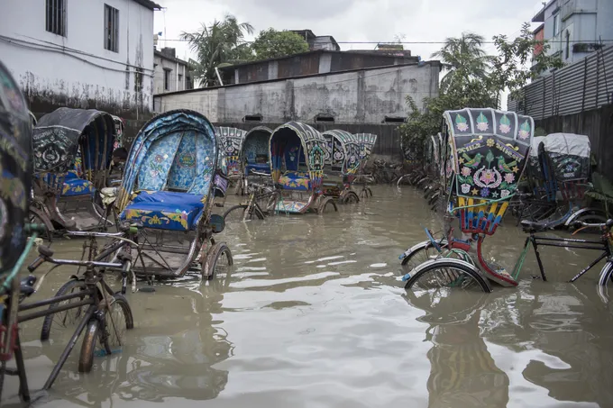 Colorful bicycle rickshaws parked in a severely flooded lot.