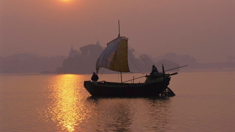 A simple, traditional sailboat silhouetted against a hazy pink sky