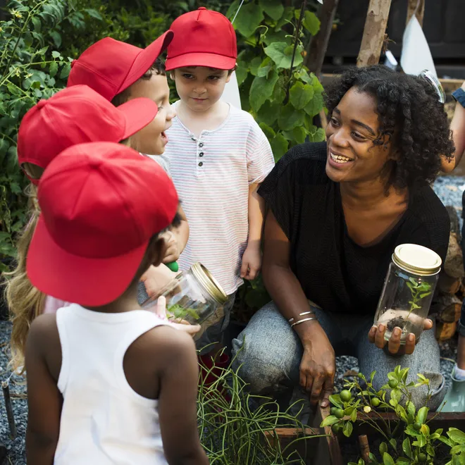 Children gather around a woman holding a plant and smiling