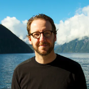 Headshot of Gerry standing in front of a majestic lake and mountains.