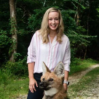 A white woman smiles and stands with a maned wolf.