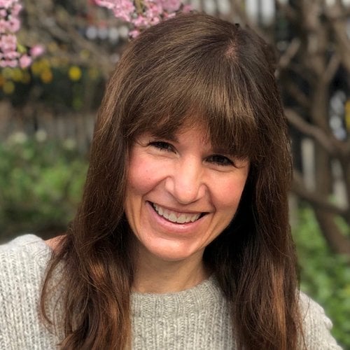 A headshot of a smiling woman in front of flowering plants