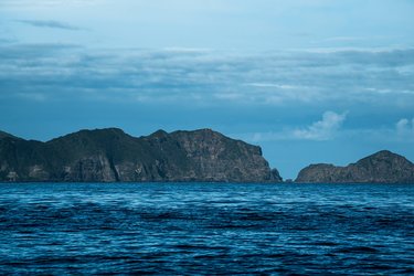 A landscape photo with a dark blue sea in the foreground, rock formations and clouds in the background
