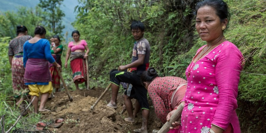 A group of people standing on a mountainside digging with a woman in all pink standing in the forefront looking at the camera