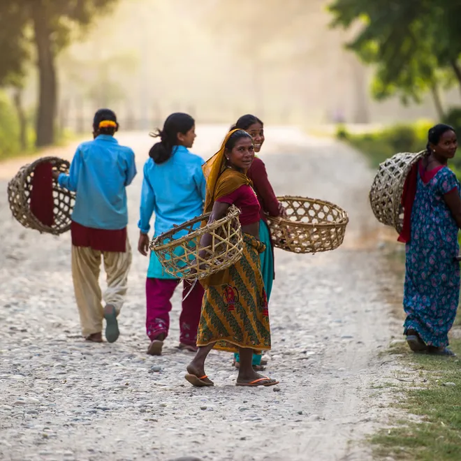 Women carry baskets and wear colorful clothes as they walk down a path