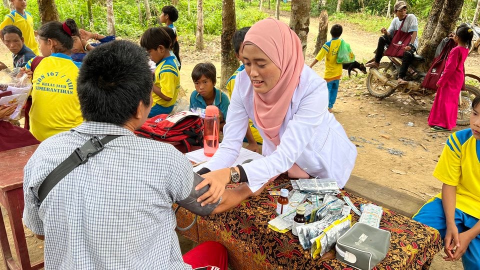 Herni reaches across a table to take someone's blood pressure