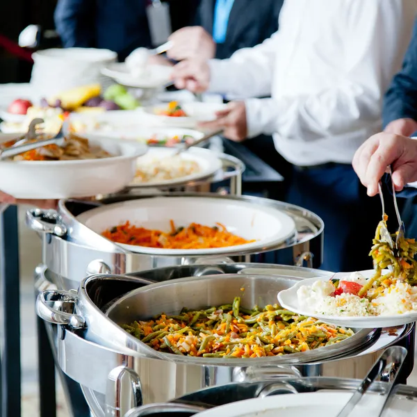 People use tongs to take food from catering trays in a hotel