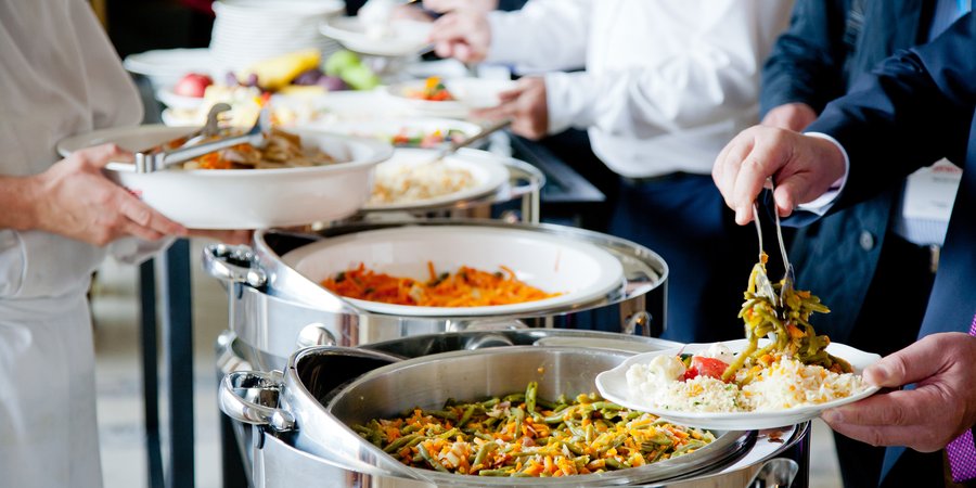 People use tongs to take food from catering trays in a hotel