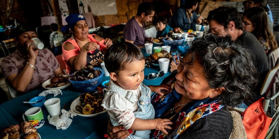 Generations of Huilliche families enjoy a curanto around a table