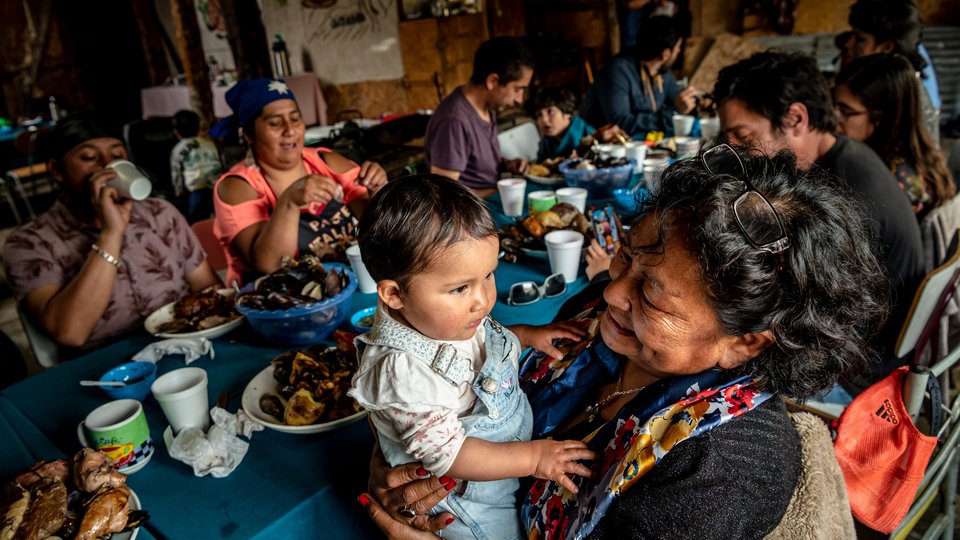 Generations of Huilliche families enjoy a curanto around a table