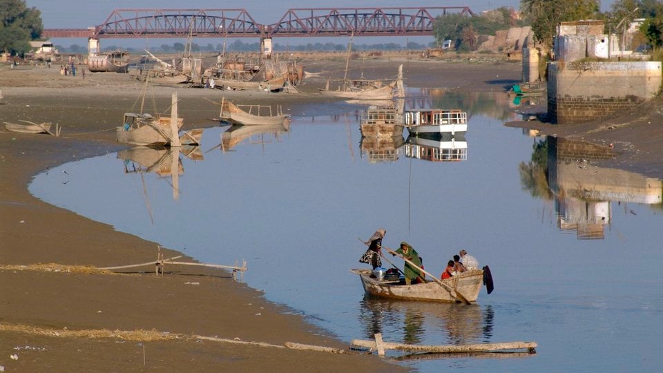 Very low river with abandoned boats and people rowing in shallow water