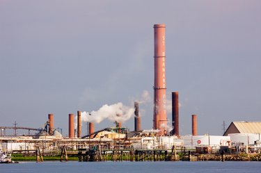 Industrial factory on waterfront along the Mississippi River in New Orleans. White emissions steam out from the rusty red metal towers.