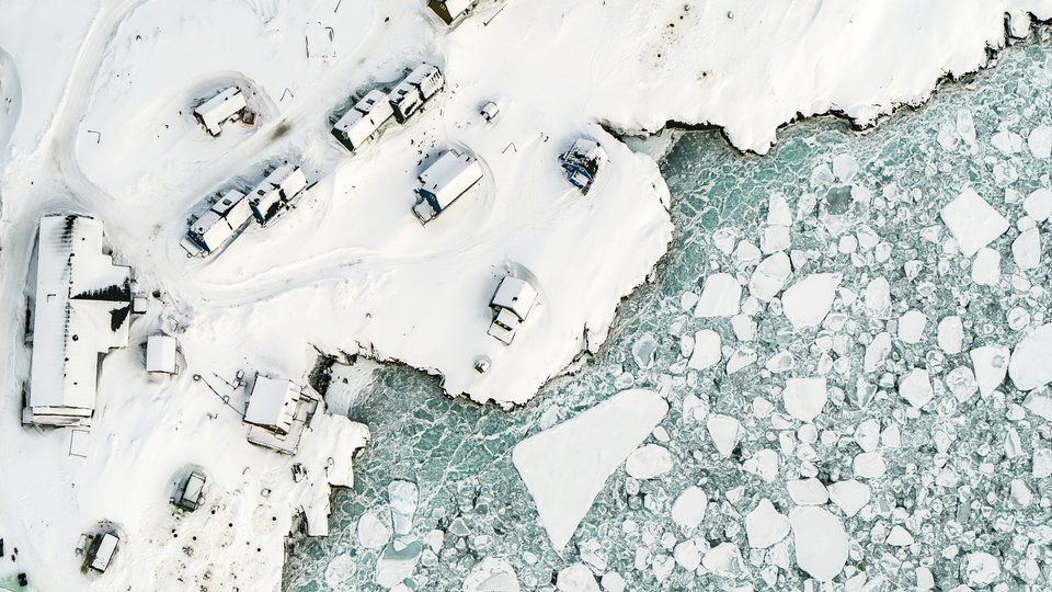 An aerial color photograph showing a landscape with icy water meeting land covered in snow