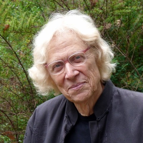 A headshot of an older person in front of green vegetation