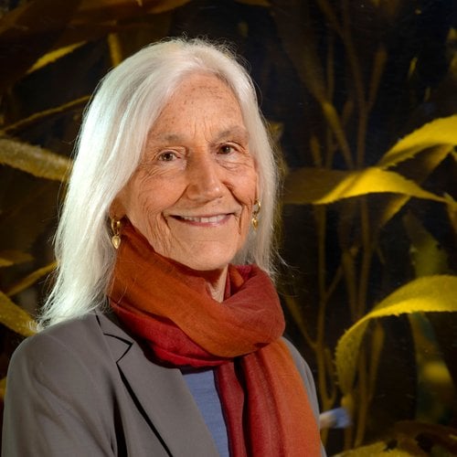 A headshot of a smiling older woman in front of plants