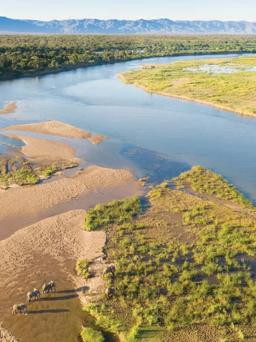 Wide angle aerial photo showing elephants crossing river in foreground and mountains in background