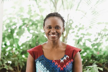 Nelly Kadagi smiles at the camera wearing a brightly patterned dress and foliage behind her