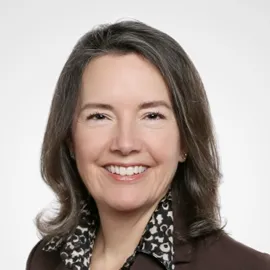 Headshot of Kathleen smiling. She has shoulder-length brown hair and is wearing a suit.