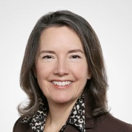 Headshot of Kathleen smiling. She has shoulder-length brown hair and is wearing a suit.
