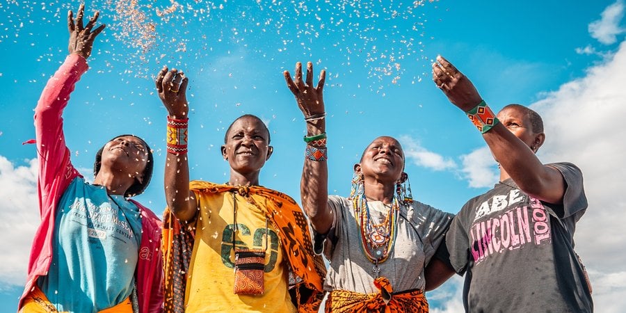 Four people in colorful clothing smiling and tossing seeds into the air