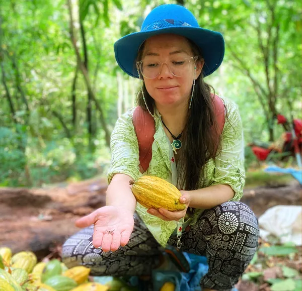 Krystal Bedregal Flores, wearing a blue hat and glasses shows an insect found on a cocoa pod.